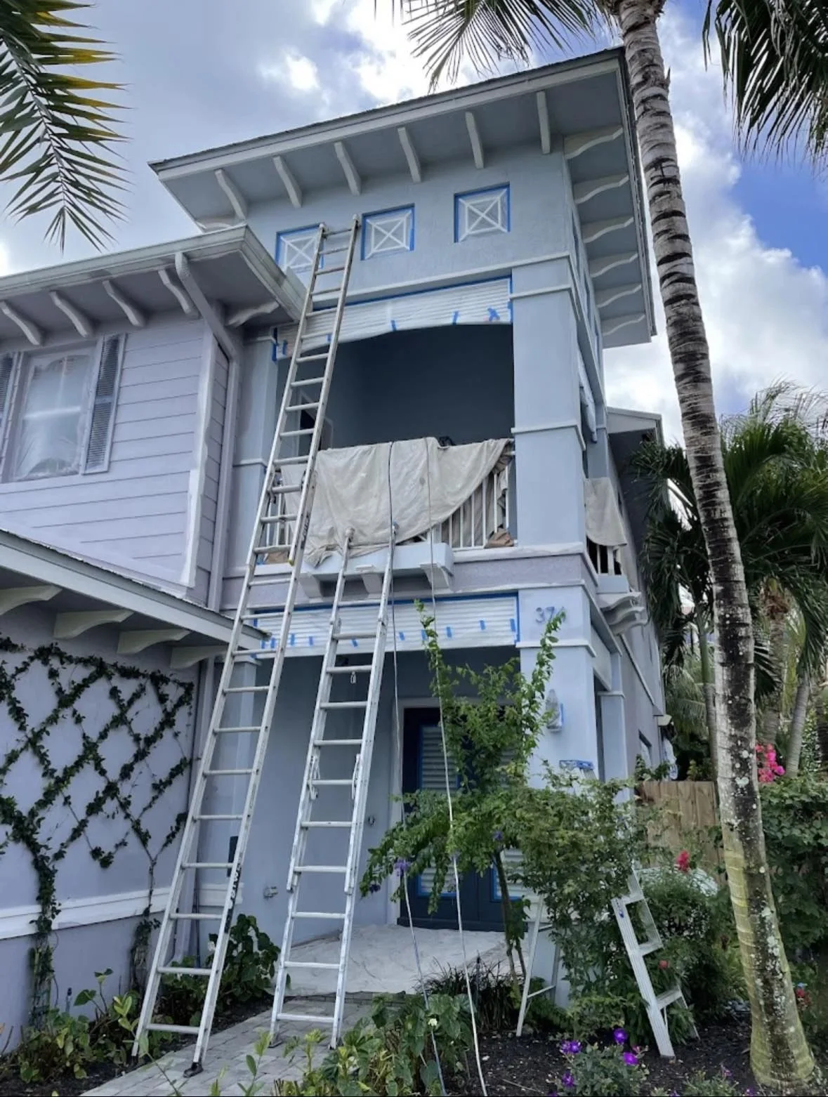 Frontline Painting crew prepping a residential exterior repaint with ladders against a blue home